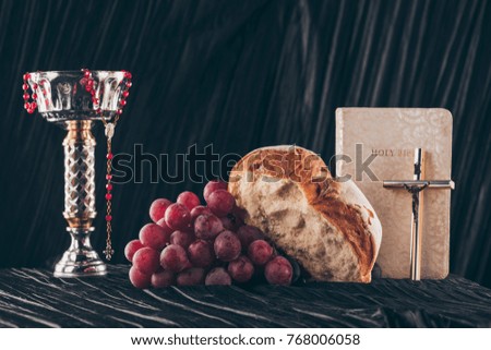 bread, grapes, bible, chalice and christian crosses on dark table for Holy Communion