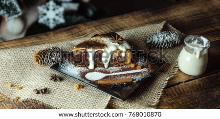 Christmas cake with white cream on wooden table with Christmas tree in background and candle