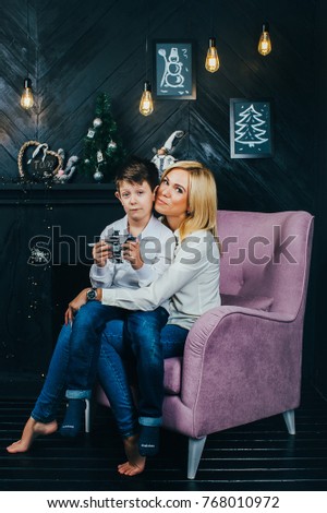 young happy mother playing with her son at the fireplace. Christmas. The room is decorated with garlands and light bulbs