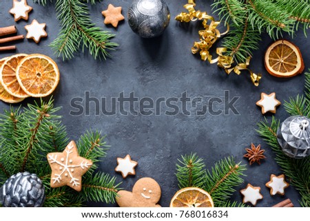 Christmas or New Year frame with fir tree branches, gingerbread cookies, spices, dried orange rings and Christmas toys on stone background. Copy space for text. Design mock up or background
