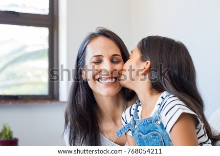 Young daughter kissing mother on cheek. Multiethnic little girl giving kiss to happy mother. Lovely daughter kissing cheerful mother on cheek at home.