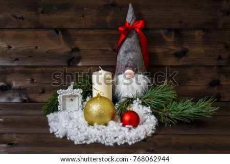 Christmas decoration with pine branches, white candle, picture frame, shiny Christmas balls, snow & scandinavian traditional gnome tomte, nisse, tomtenisse, tonttu with red ribbon on wooden background