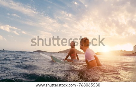 Fit couple surfing at sunset - Surfers friends having fun inside ocean - Extreme sport and vacation concept - Focus on man head - Original sun color tones Royalty-Free Stock Photo #768065530