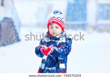 Preschool kid boy in colorful clothes playing outdoors during strong snowfall. Active leisure with children in winter on cold snowy days. Happy child having fun, playing with snow. Winter fashion