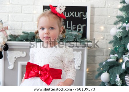 Cute little girl in a dress against a white fireplace with and Christmas tree, New Year's Day