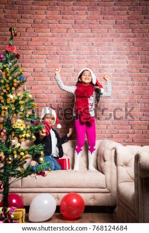 cute little Indian kids with gift boxes on christmas, sitting on floor or sofa with christmas tree in the background