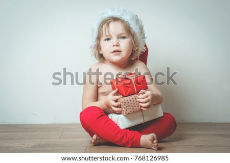 Portrait of child in Santa red hat with Christmas gifts in hands. Smiling funny kid at Christmas night. Cute kid with many Christmas presents.