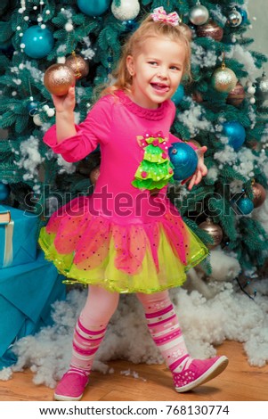 Blonde cute little girl sitting and smiling nearly decorated christmas tree and new year presents