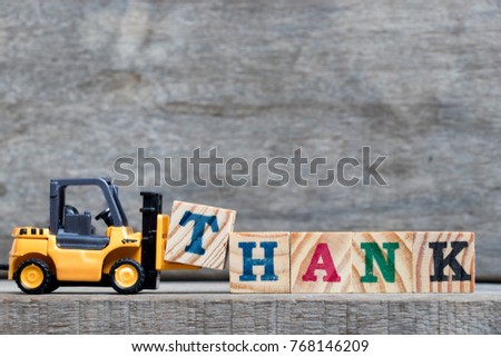Yellow plastic forklift hold letter T to complete word thank on wood background
