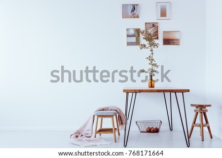 Orange vase with branch on table in simple dining room with stools and pictures on a wall with copy space