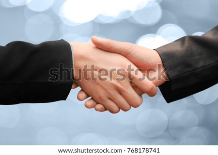 Businessman wearing a black suit shake hands while two successful on blue background.
