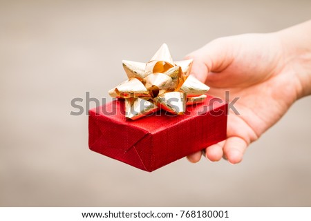 Woman hand hold a red gift box tied with golden ribbon for give in the public park, present for Christmas and new year and valentine day or Important occasions concept.