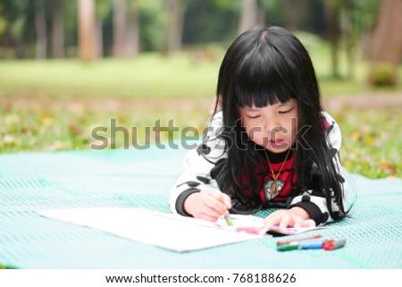 Asian children cute or kid girl learning for coloring or sleep drawing paint on green mat and nature meadow at garden or public park for fun and preschool education on holiday relax