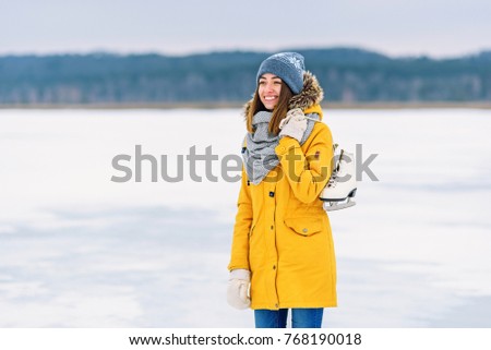 Beautiful girl in a yellow winter jacket with ice skates in the middle of a frozen lake.