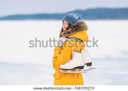 Beautiful girl in a yellow winter jacket with ice skates in the middle of a frozen lake.