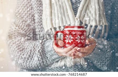 Girl in knitted sweater with a mug in hands on snowy background. Winter warming up concept. Close up.