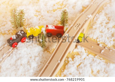 Wooden children's train rides between the trees. The white flakes of artificial snow lying on the toys. The concept for the decoration of a showcase of a toy store. Railway in miniature