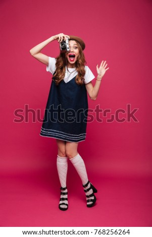 Full-length shot of shocked lady making photo with retro camera isolated over pink