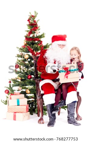 Cute little girl receiving gift from Santa Claus sitting on his lap near Christmas tree