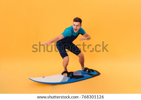 Picture of a Happy surfer in wetsuit using surfboard like on wave over yellow background