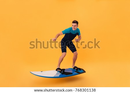 Picture of a Smiling surfer in wetsuit using surfboard like on wave over yellow background