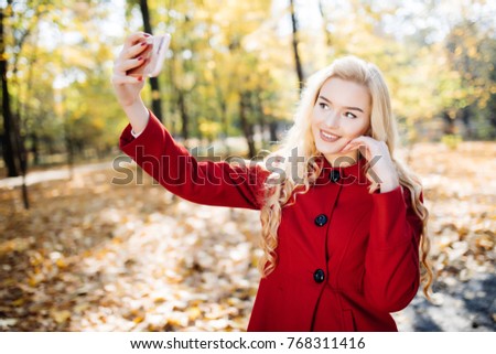 Teenage girl in autumn in park taking a selfie on smart phone. Beautiful happy young woman taking a photo of herself outdoors