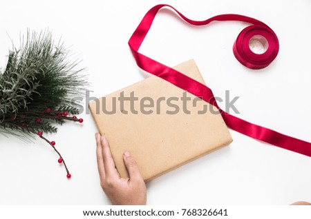 Woman's hands wrap christmas holiday handmade present in craft paper with red ribbon.