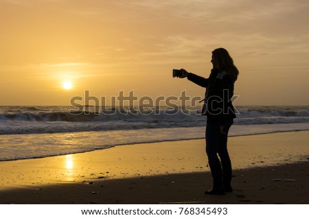 Backlight of single woman walking and taking pictures with the mobile
