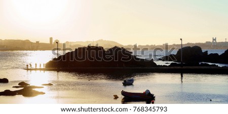 Sunset against the light with the Coruna sky line in the background with people fishing in a small port and anchored boats nearby