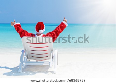 Santa Claus relaxing on chaise longue and celebrating Christmas on sandy beach, sea background with copy space. Concept of enjoy winter holidays at tropical destination.