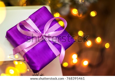 Christmas present in purple packing with satin ribbon on Christmas tree