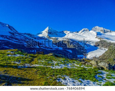 high altitude austrian alp landscape on a very sunny day with blue sky with green grass in front and a very unique and lonely standing mountain all covered with ice and snow