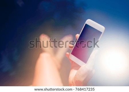 Woman holding smartphone over the swimming pool in bright sunlight
