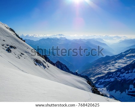 the view down from an snow covered mountain side in the austrian alps deep in a long and narrow valley with little fog below a clear blue sky on a very sunny day