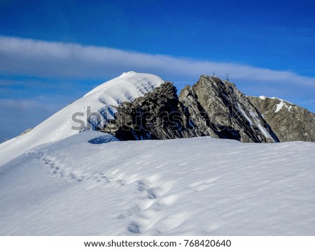 the last meters of an high altitude mountain ridge in the austrian alps, all covered with snow and the summit seen in the background, all below blue sky