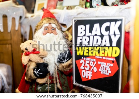Santa Claus or Father Christmas dummy figure or mannequin on display holidng a teddy bear in a toy shop window next to a 25% off Black Friday sign in the UK