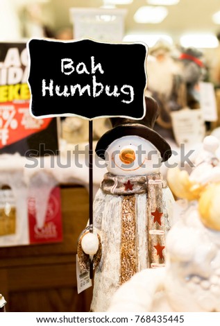 Ornamental snowman wearing a scarf, coat and a top hat holding up a Bah Humbug sign in a Christmas shop in the UK