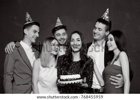 Birthday concept. Group of very cheerful friends in birthday hats celebrating a birthday and posing in front of the camera on a festive background with cake. Black and white photo