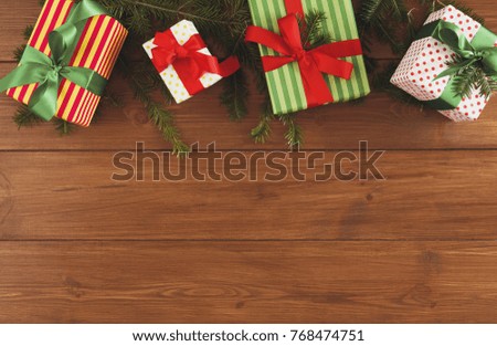 Christmas gift boxes and fir tree twigs border, top view with copy space on wood table background. Frame of colored packages with ribbons.