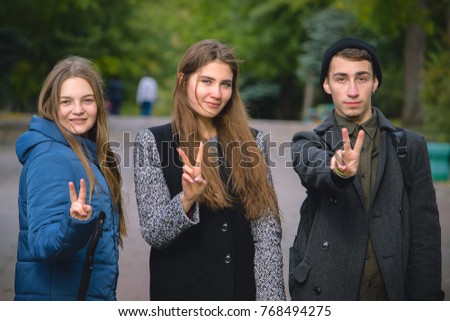 Teens in casual shirt is fooling around, posing and shows v sign, smiling on wall background