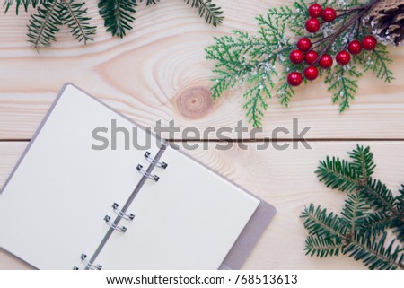 Christmas light wooden background with fir tree branches, a branch with red berries and a notebook. Top view. Close up. Copyspace