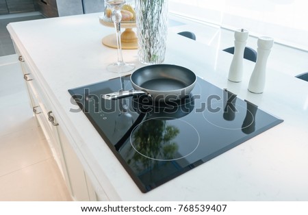 Frying pan on modern black induction stove, cooker, hob or built in cooktop with ceramic top in white kitchen interior Royalty-Free Stock Photo #768539407