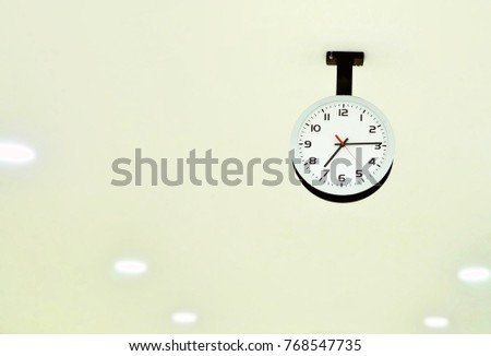 object image of white vintage clock hang on ceiling with lamp light blur background.