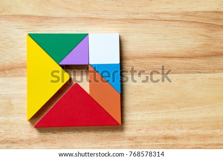 Color tangram puzzle in square with arrow inside shape on wood background