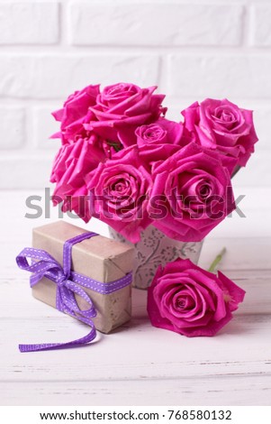 Bright pink roses flowers in pot  and box with present  on white  wooden background. Selective focus. Vertical image.