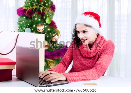 Picture of young woman shopping online by using a computer laptop while sitting near Christmas tree