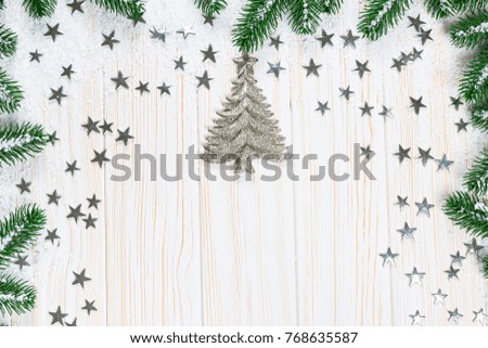 Christmas fir tree in snow with silver stars and New Year decor toy on white wooden background. Free space. Winter frame