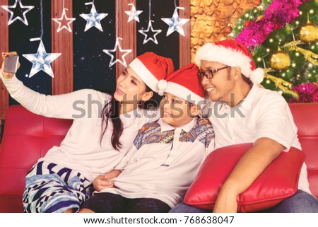 Young parents taking a selfie photo with their son while sitting on the couch. Shot at Christmas time