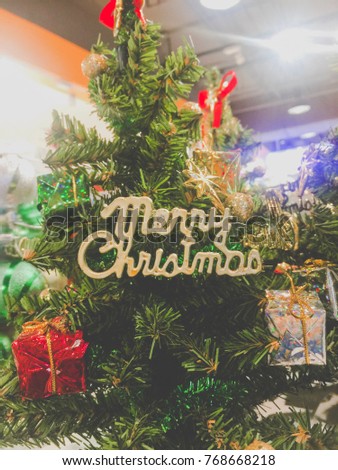 Image of a little Christmas tree with many ornaments like gifts and bow with a very big merry Christmas sign in the middle.