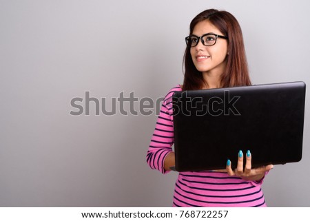 Studio shot of young beautiful Indian woman wearing eyeglasses against gray background